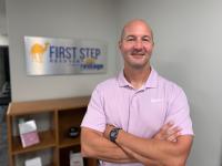 Thad Stafford standing with arms crossed in front of First Step Recovery sign